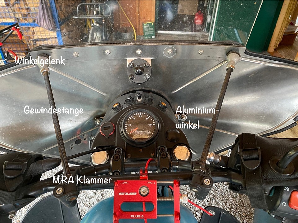 Zurück zu dem sowjetischen Windschild, es bietet einfach den besten Wetterschutz. Die obere Halterung habe ich aus geraden Winkelgelenken, Gewindestange und den MRA Klammern gebaut. In der Mitte habe ich das Schild mit zwei Aluwinkeln an der Lampenhalterung befestigt. Unten ist das Windschild mit zwei Streben an der Gabel abgestützt.